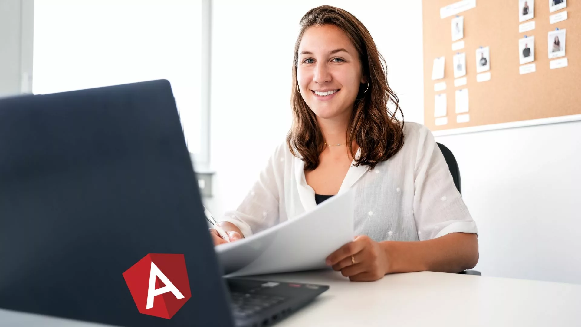 Frau sitzt an einem Tisch vor Laptop mit Angular-Aufkleber.
